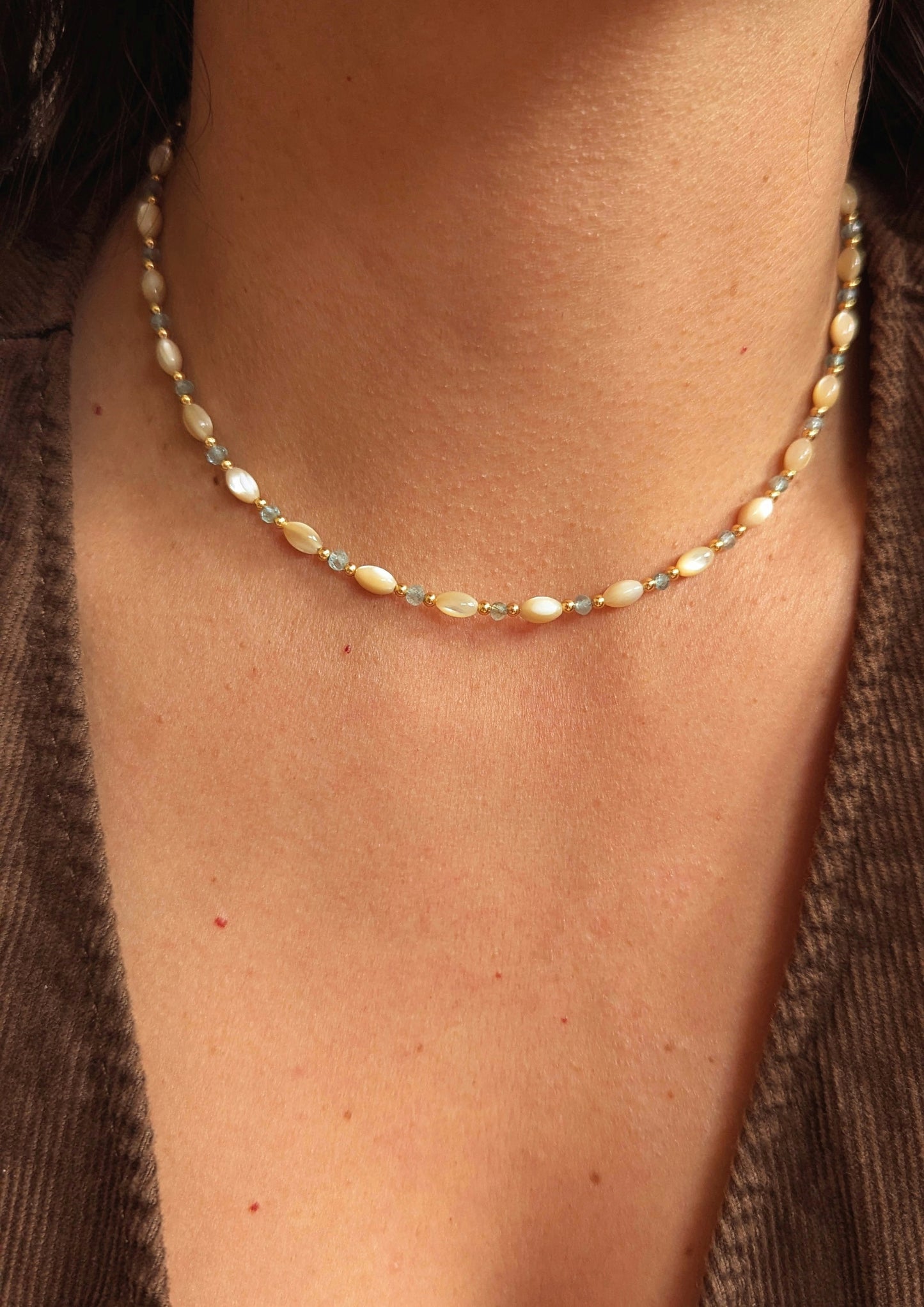 Moon & Milk's choker necklace made with mother of pearl rice beads, blue apatite stones, and gold spacers, worn as a short choker above the collarbone.
