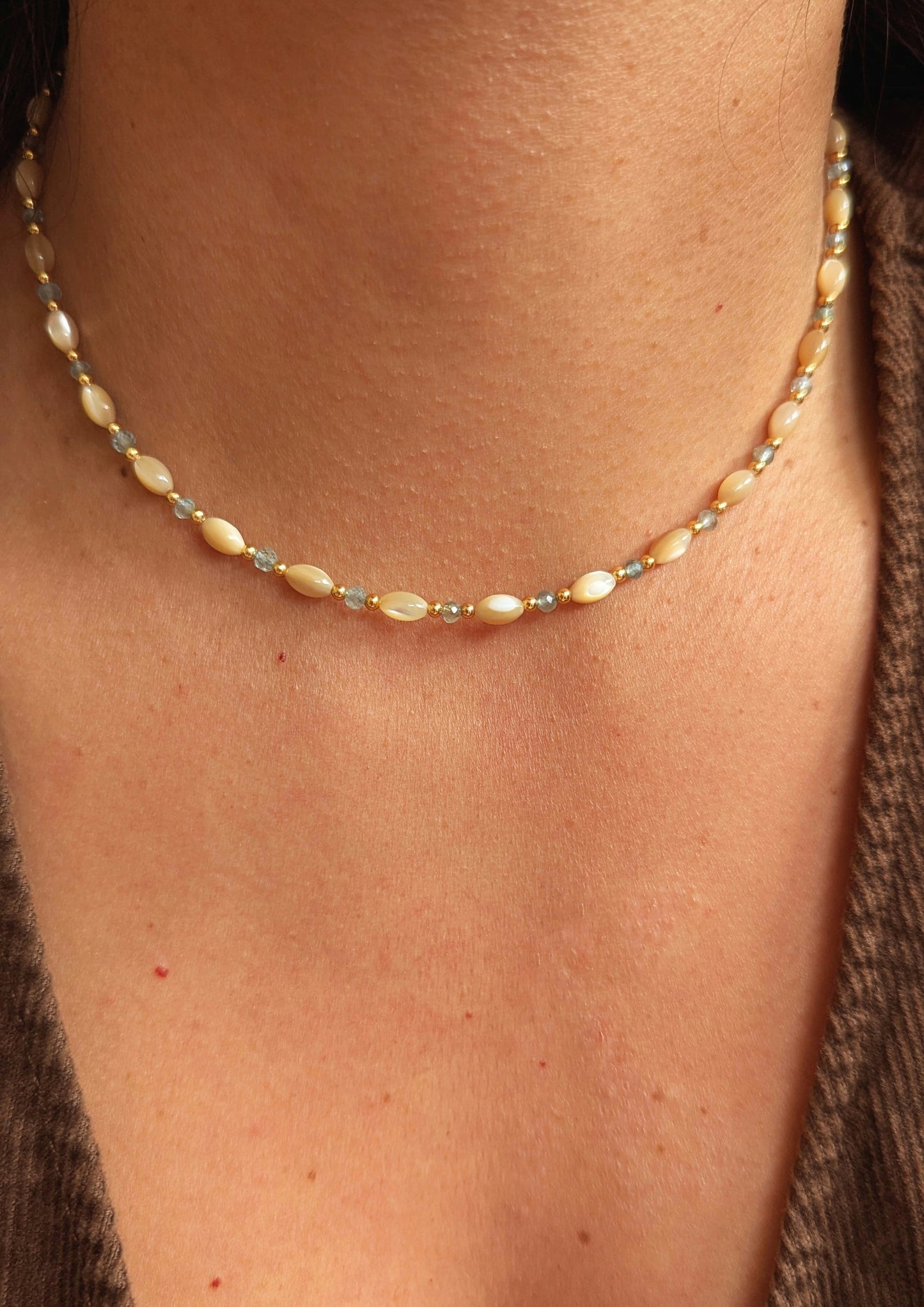Moon & Milk's choker necklace made with mother of pearl rice beads, blue apatite stones, and gold spacers, worn as a short choker above the collarbone.