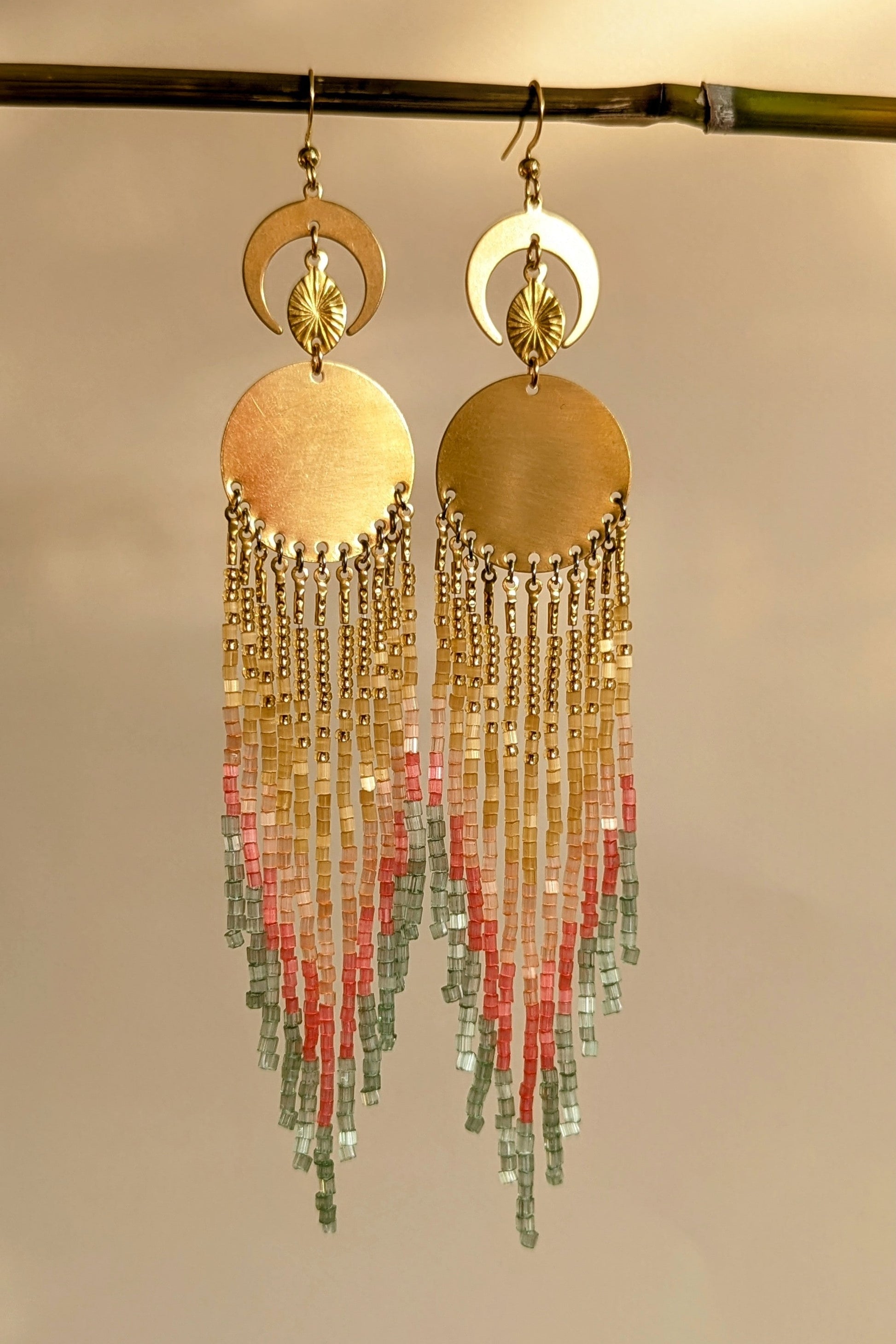 Gold beaded earrings with colorful and sparkly beaded fringes on a beige background.