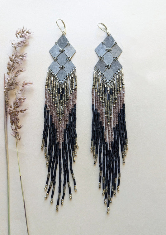 Pair of black beaded earrings with fringes on a light background.