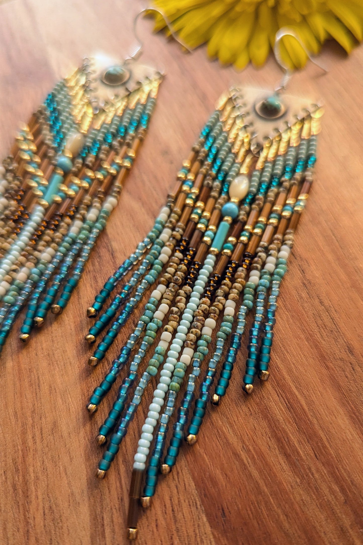 Beaded earrings with teal and gold strands on a wooden surface by Moon & Milk.