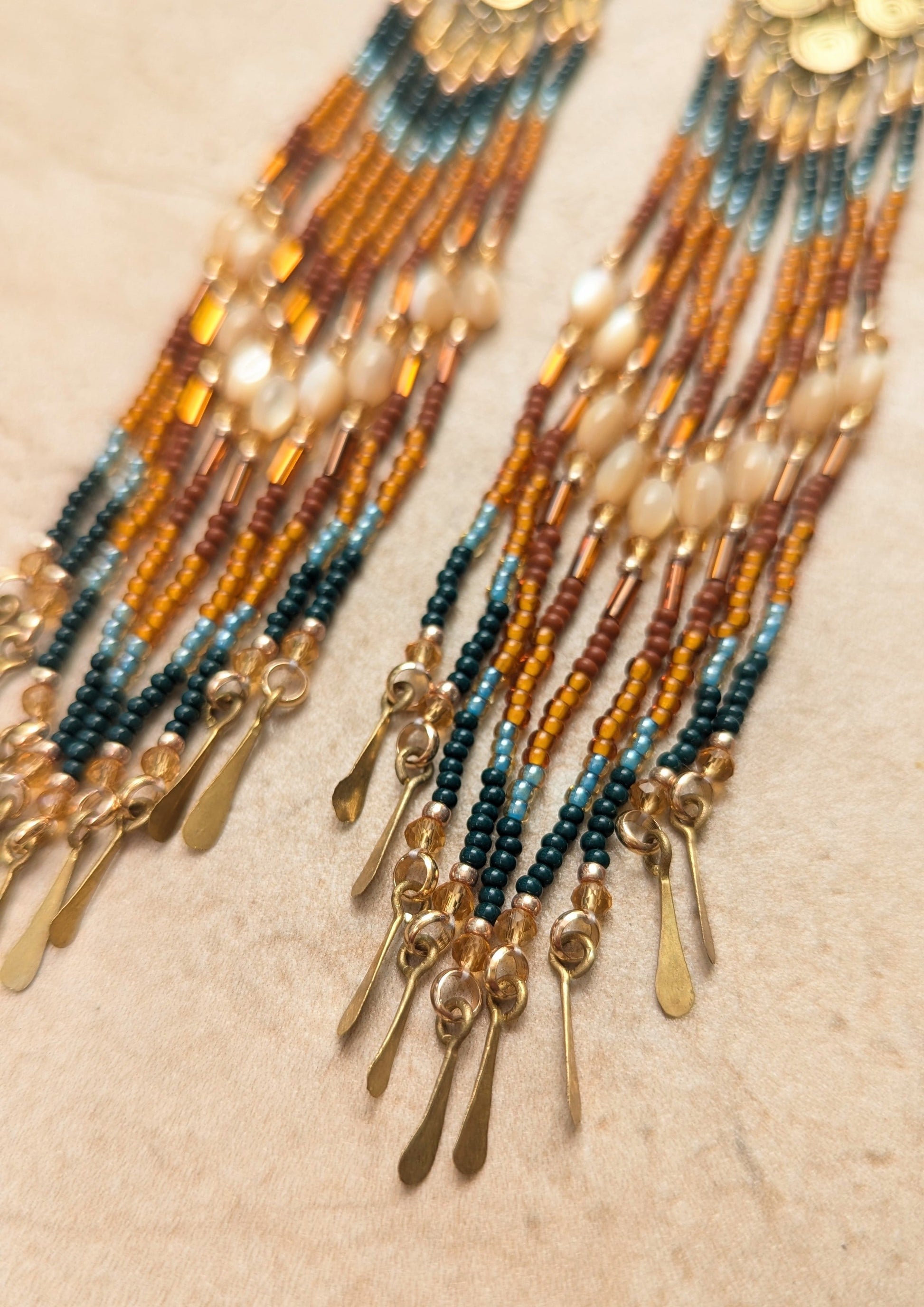 Beaded earrings with gold accents on a beige background.