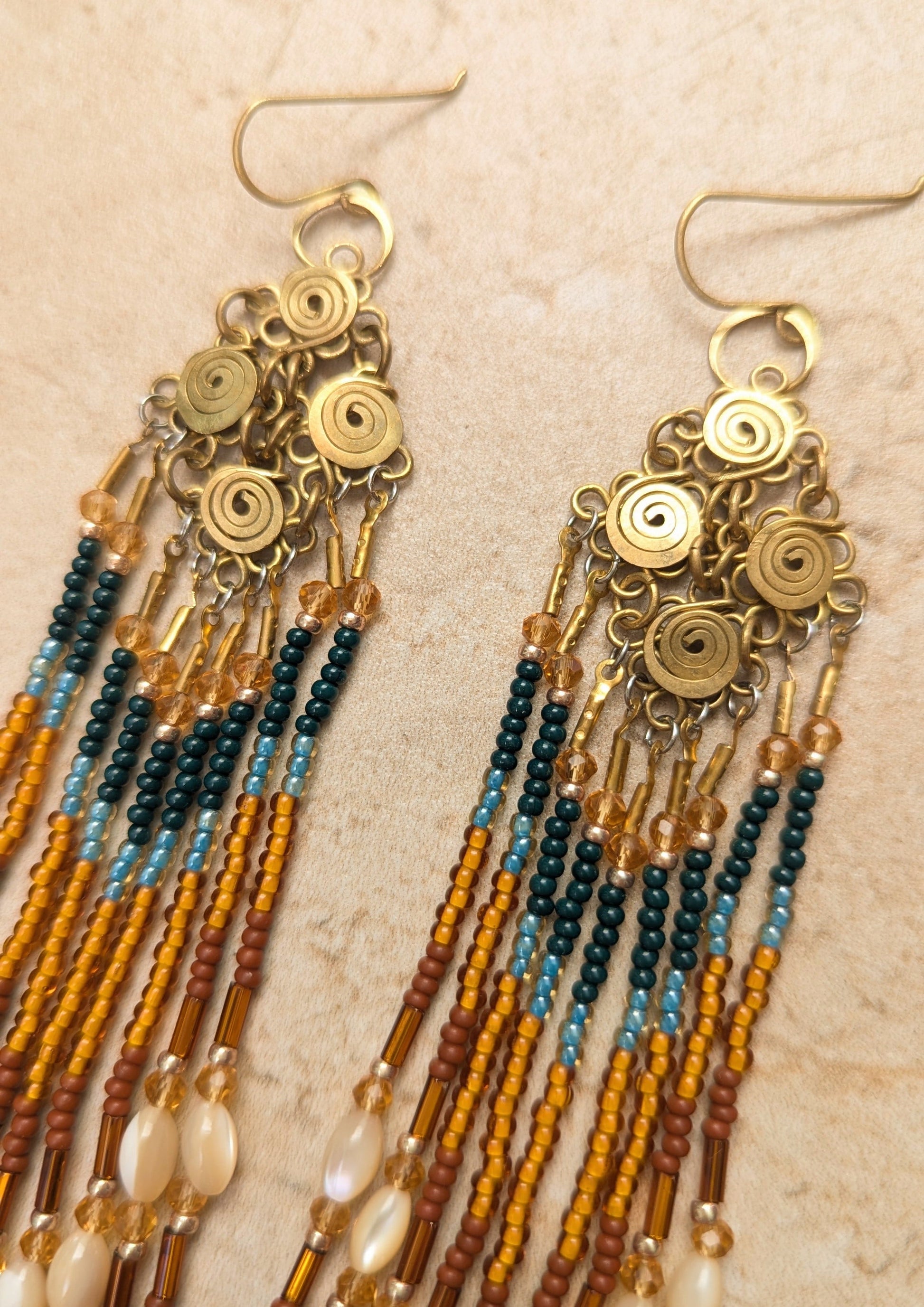 Pair of beaded earrings with brass wirework on a beige background.
