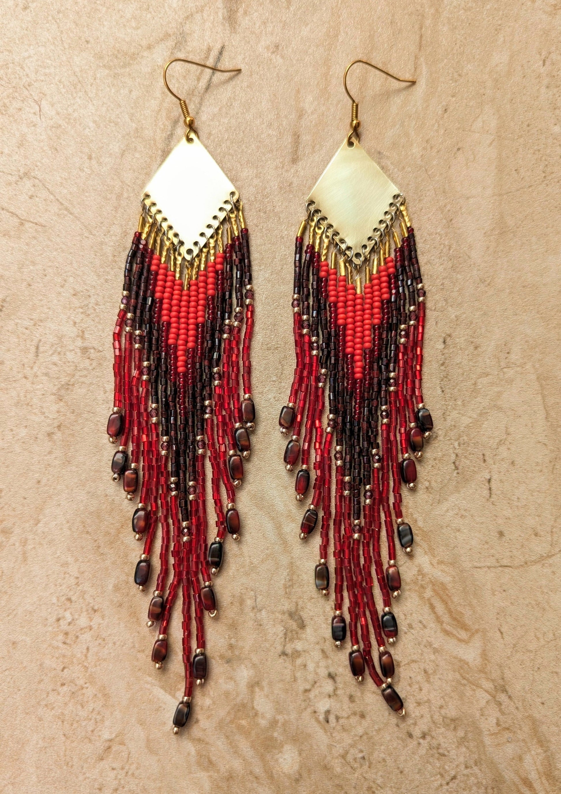 Pair of boho beaded earrings with red and black beads on a beige background.