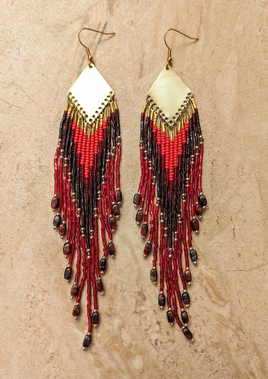 Pair of boho beaded earrings with red and black beads on a beige background.