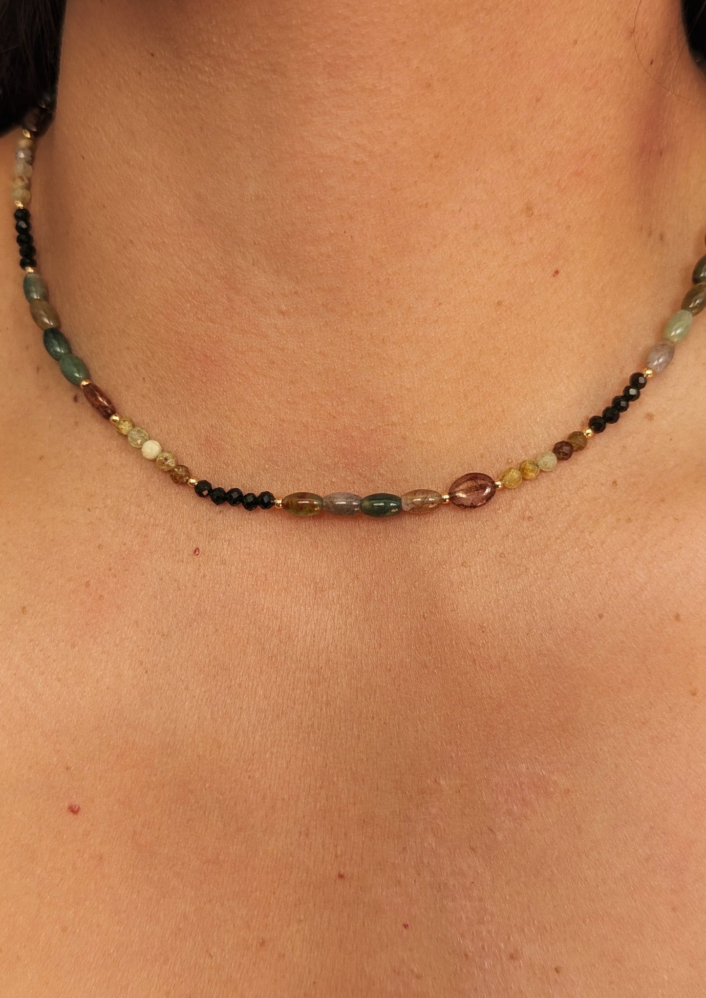 Close-up of a woman wearing a gemstone agate beaded necklace on a plain background.