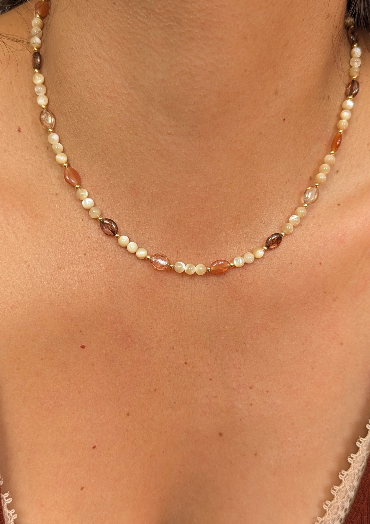 Necklace made with mother of pearl beads, 18k gold-plated spacer beads, and mixed Czech glass beads in warm neutral tones displayed on a woman.