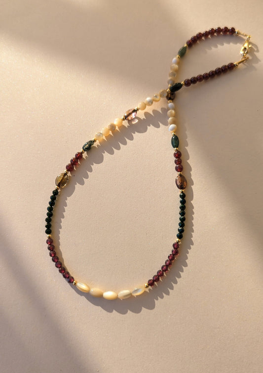 Necklace with multicolored garnet beads on a beige background.