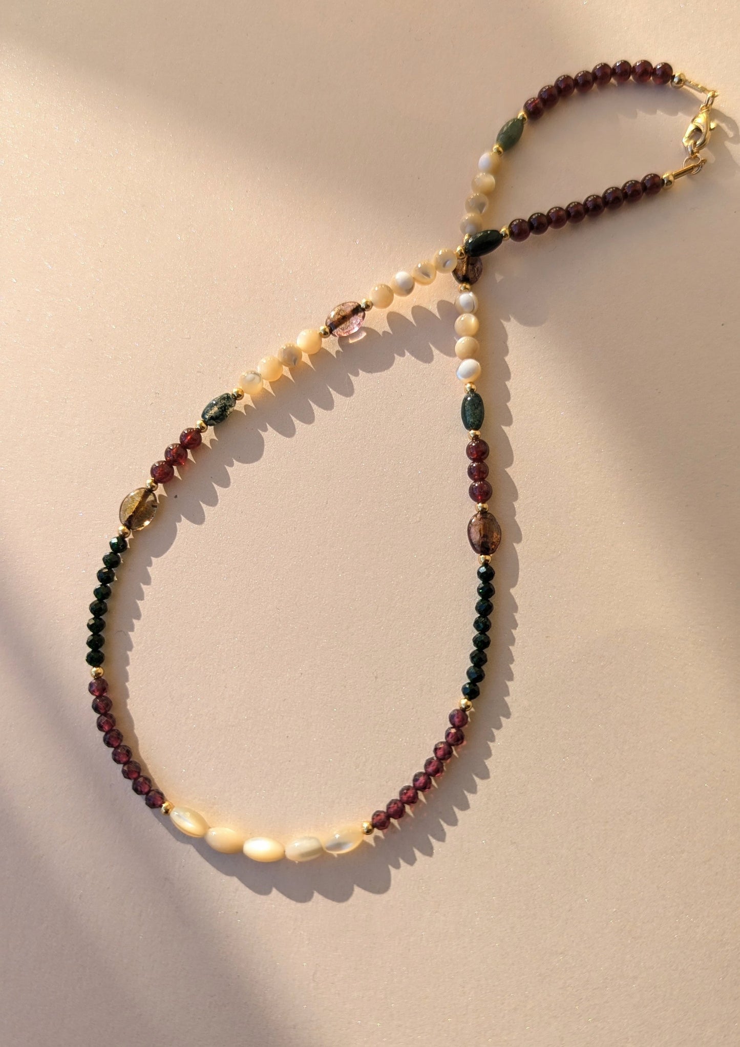 Beaded necklace with multicolored gemstone beads on a beige background.
