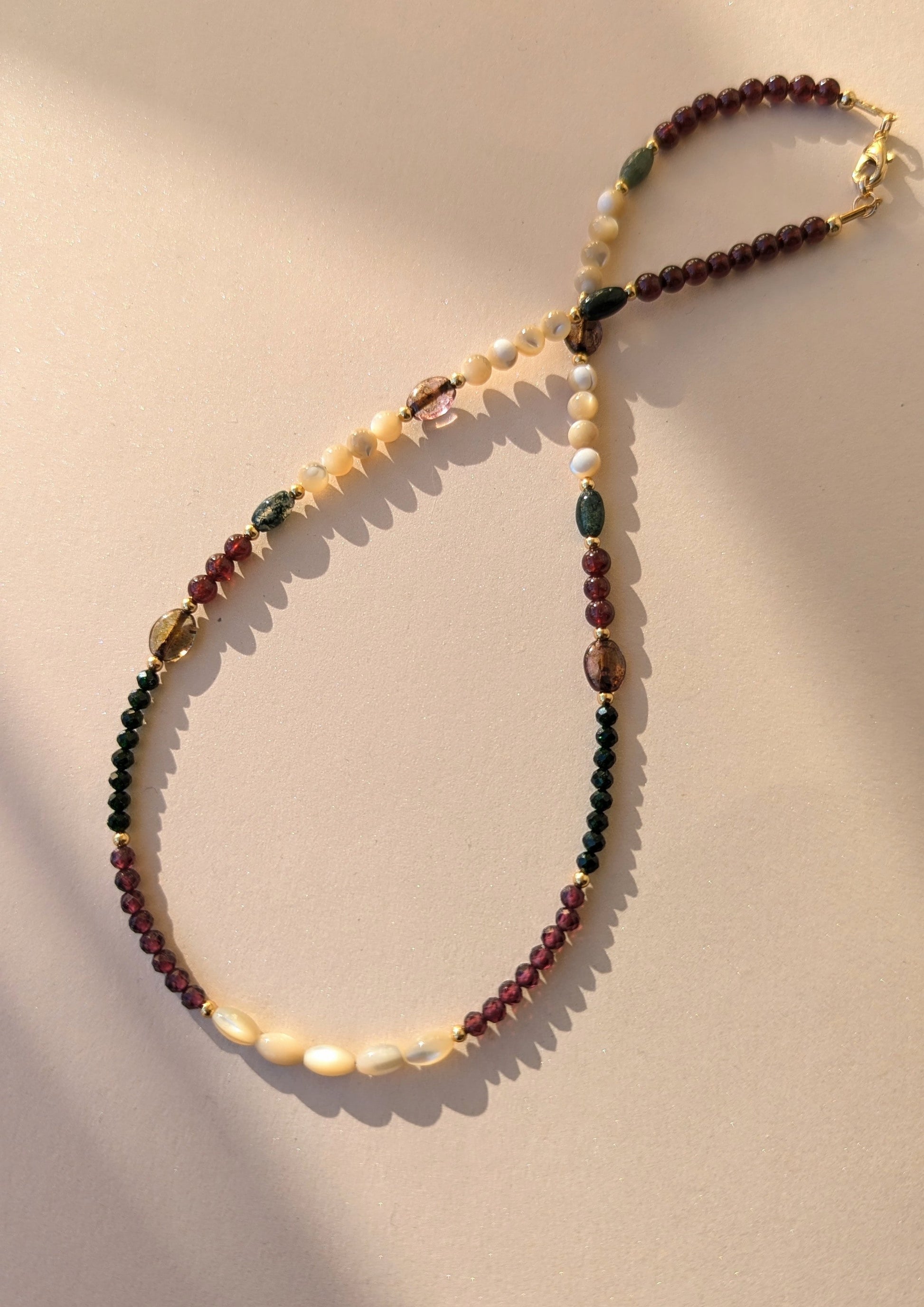 Beaded necklace with multicolored gemstone beads on a beige background.