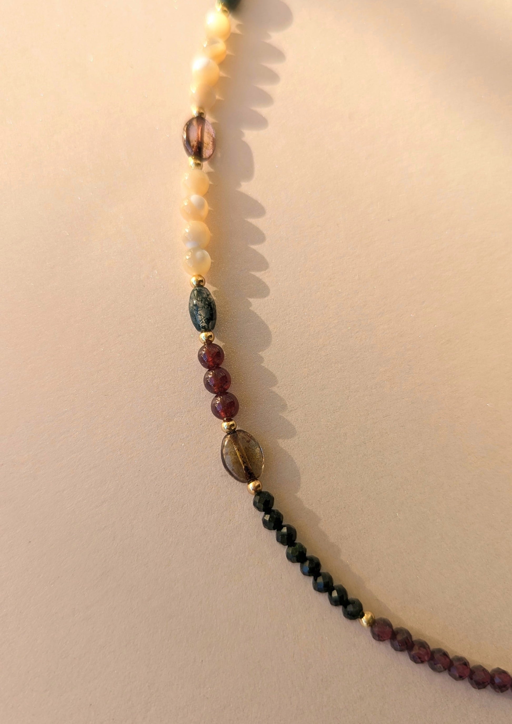 Necklace with multicolored garnet beads on a beige background.