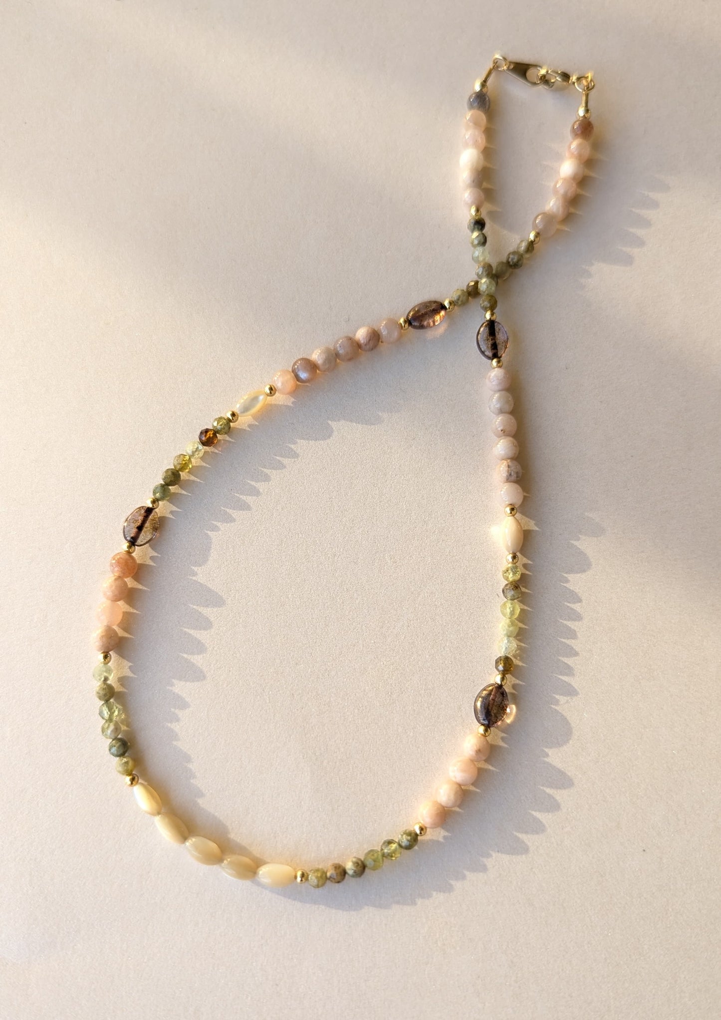 Necklace with moonstone and green garnet beads on a light background.