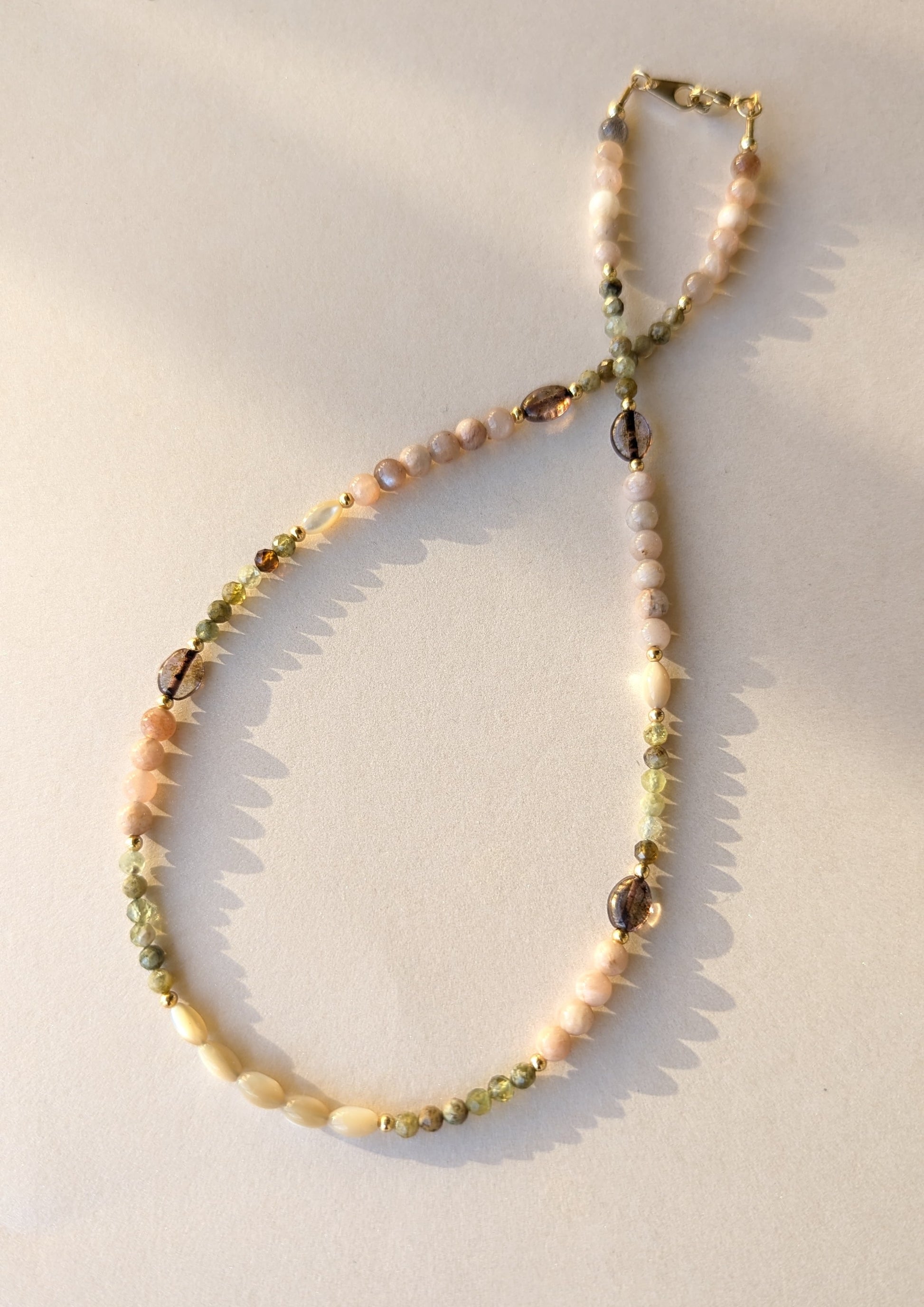 Necklace with moonstone and green garnet beads on a light background.