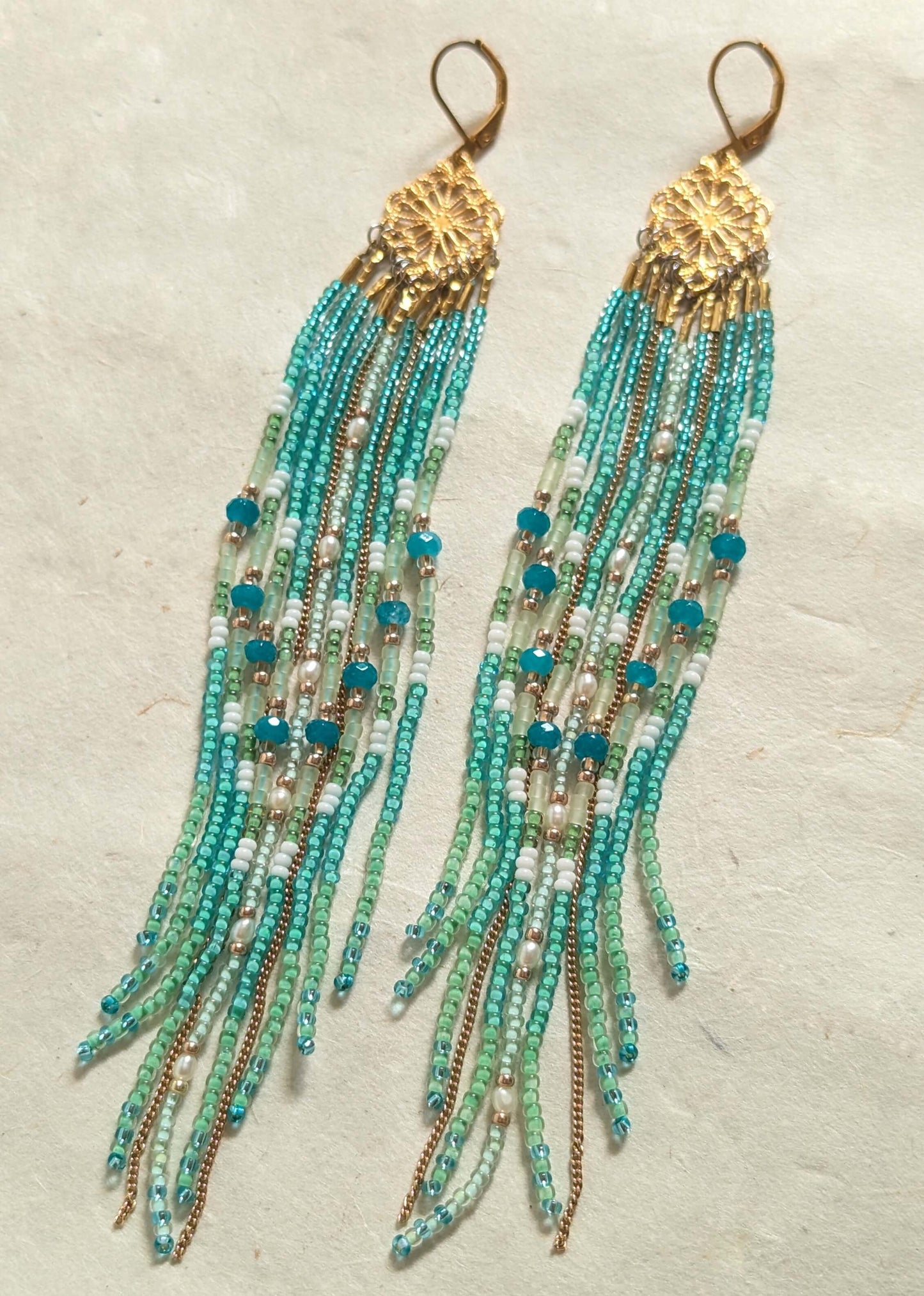 Turquoise beaded earrings with gold accents on a textured beige background by Moon & Milk. 
