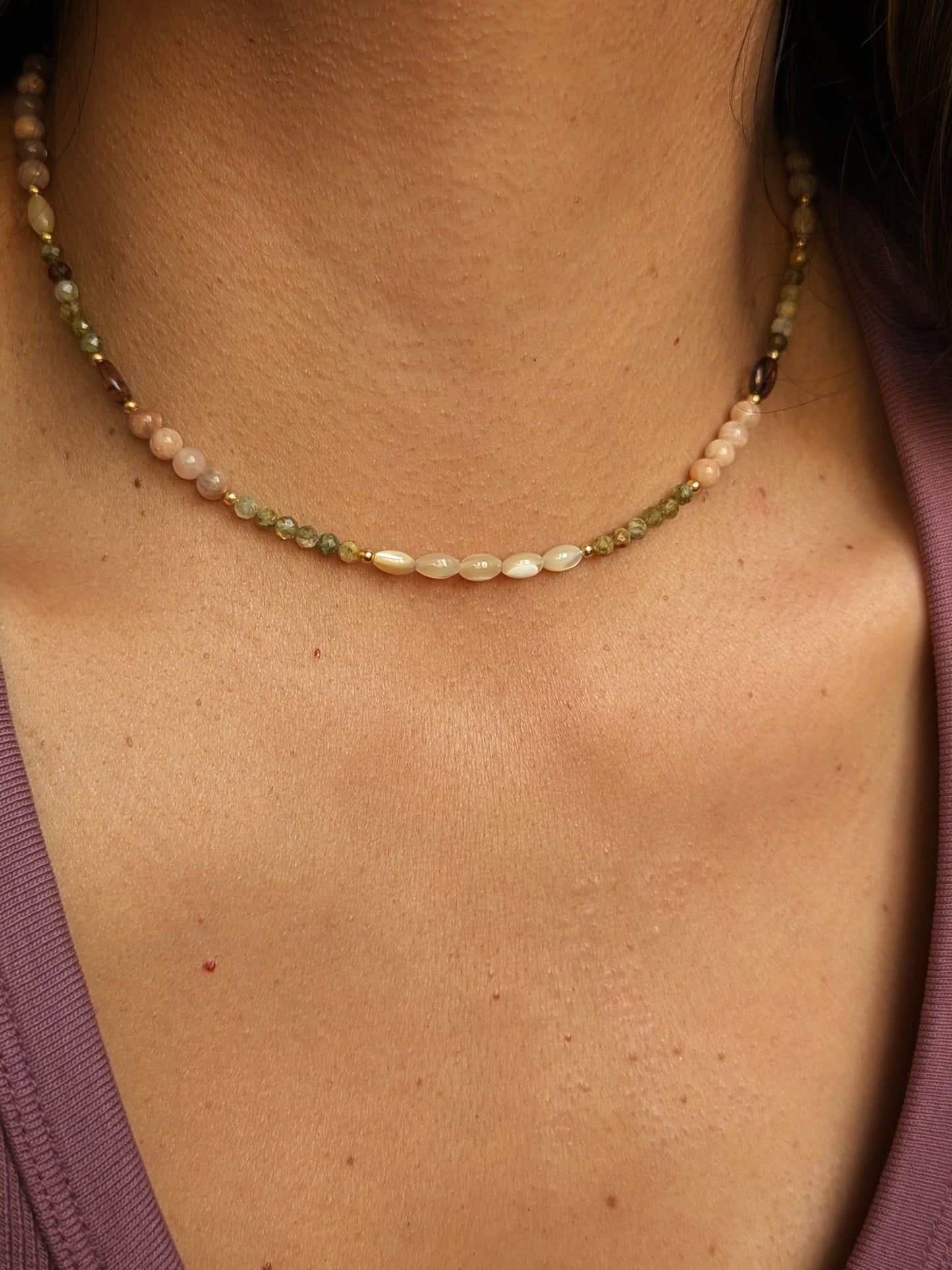Gesmtone necklace with multicolored beads and mother-of-pearl on a person wearing a purple top.