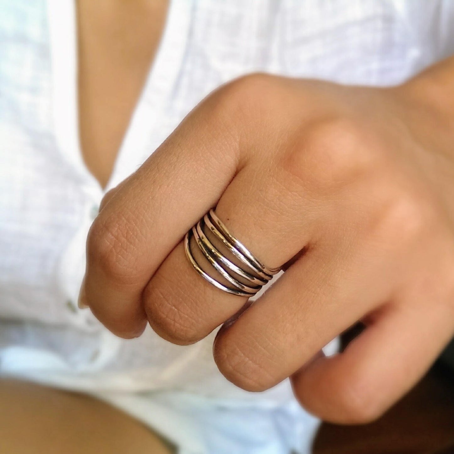 Close-up of a hand wearing a multi-band silver ring on a blurred background
