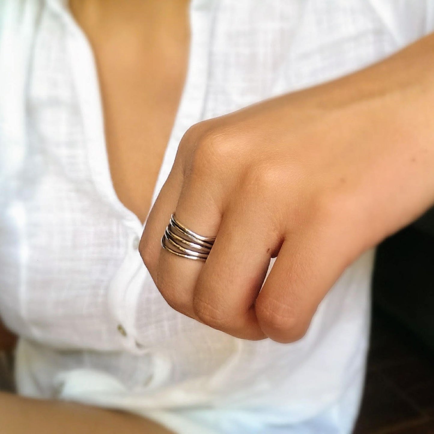 Close-up of a hand wearing a silver ring with a blurred white background