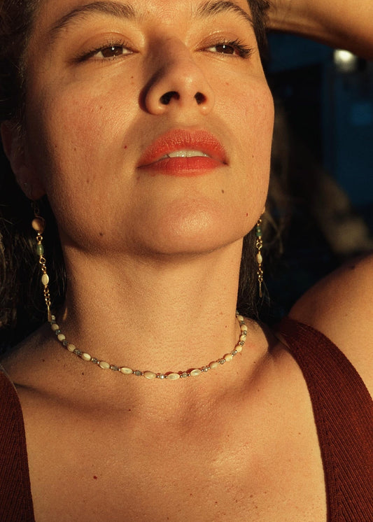 Close-up of a woman with red lipstick and a mother-of-pearl beaded necklace, with a blurred background.