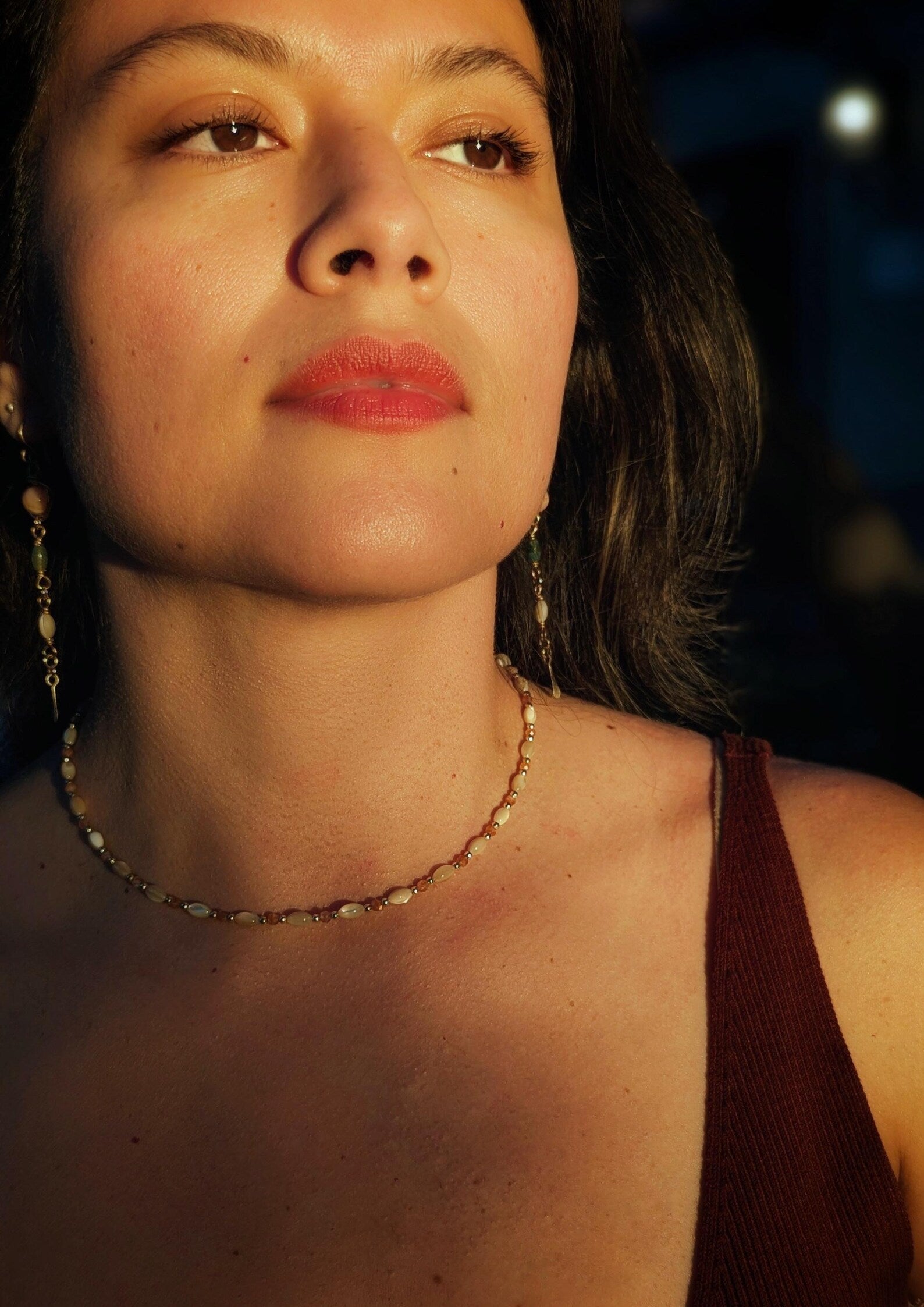 Close-up of a woman's face wearing a mother-of-pearl and sunstone necklace with a blurred background.
