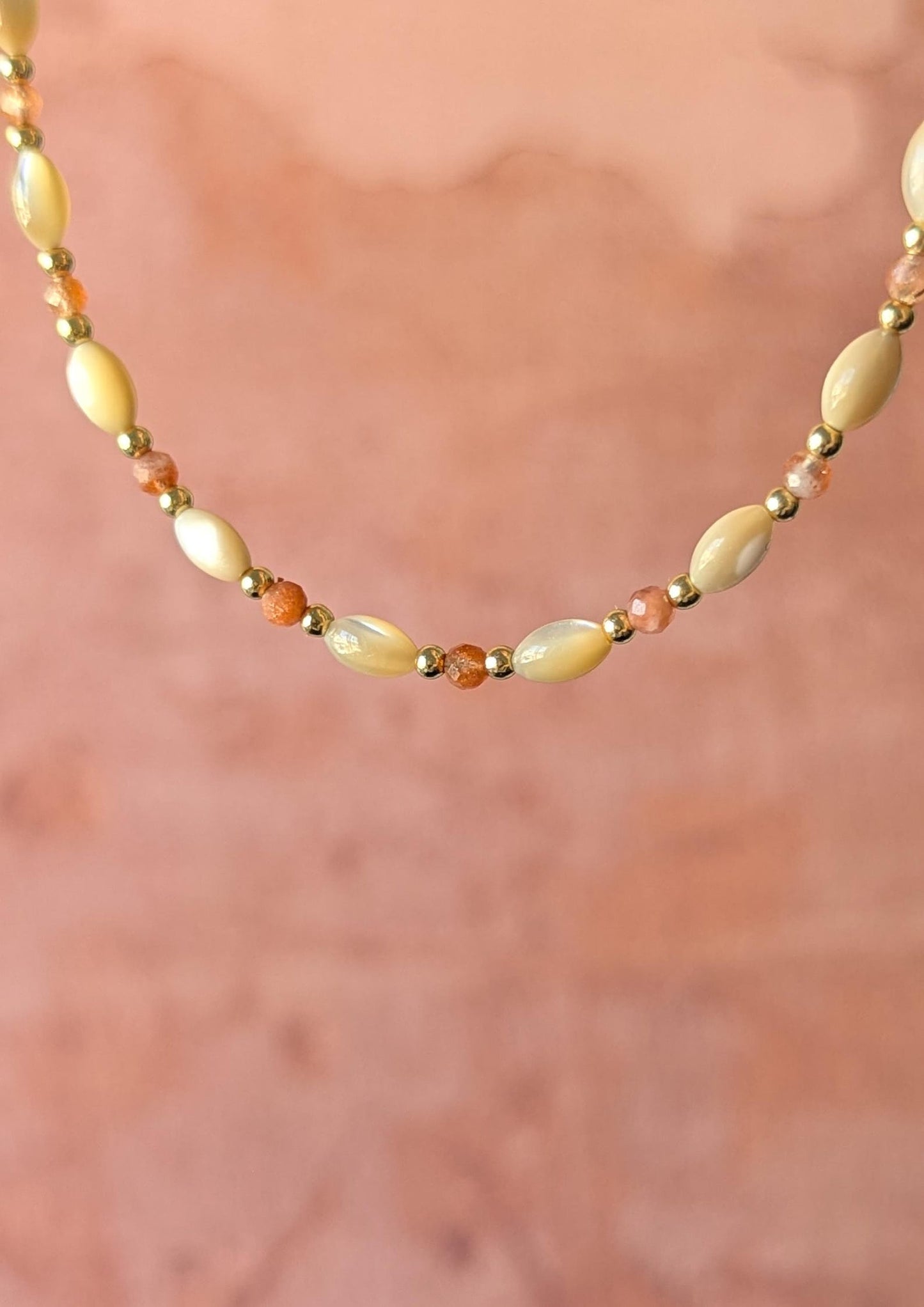 Necklace with mother-of-pearl rice beads and faceted sunstone on a soft pink background.