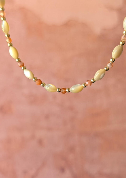 Necklace with mother-of-pearl rice beads and faceted sunstone on a soft pink background.
