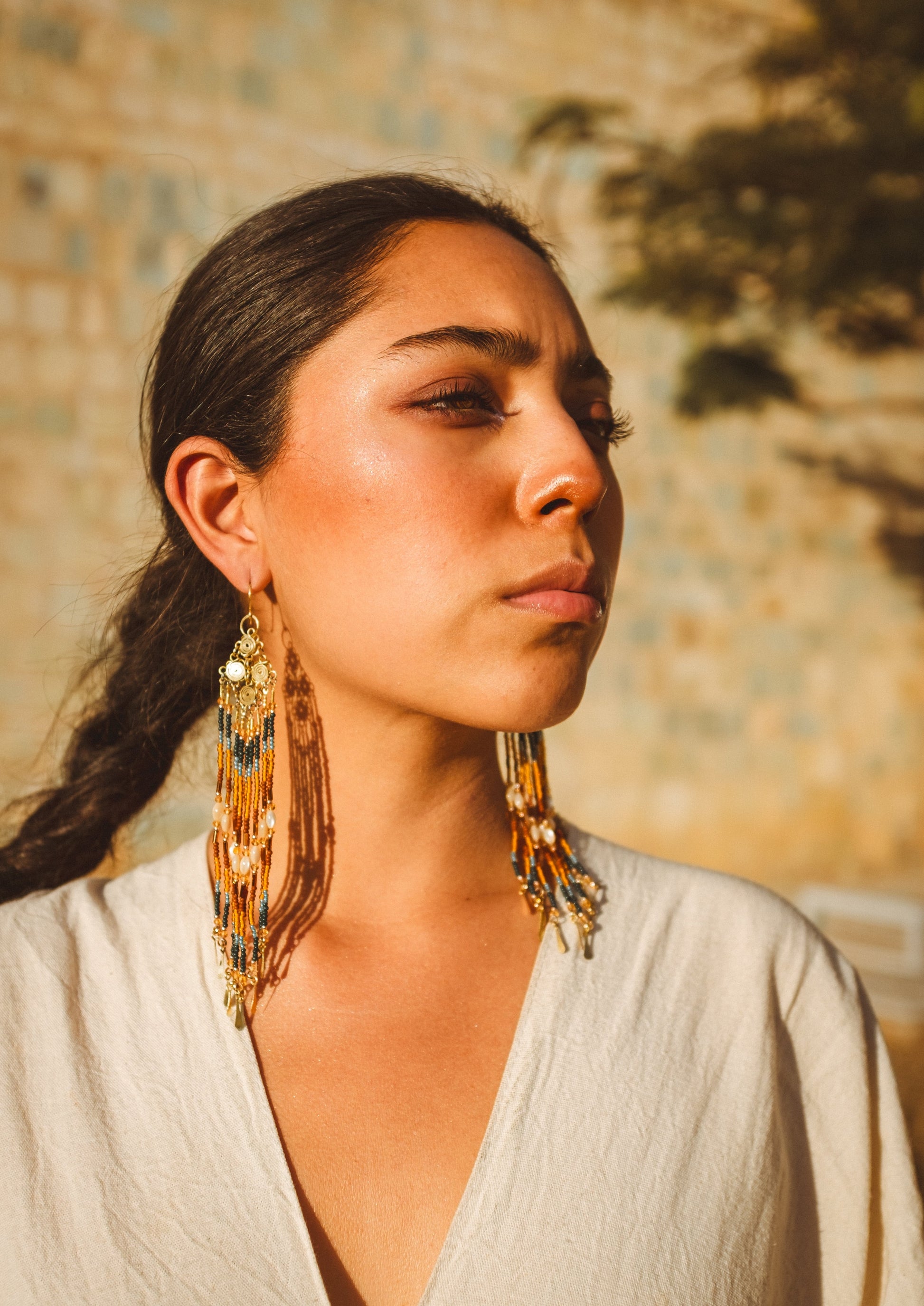 Woman wearing large, ornate  beaded earrings with a warm, blurred background.