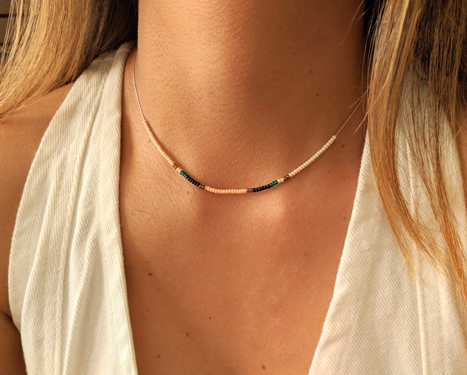 Delicate choker necklace with tiny pastel and dark beads, elegantly displayed on a woman's neck, paired with a white sleeveless blouse for a refined look.