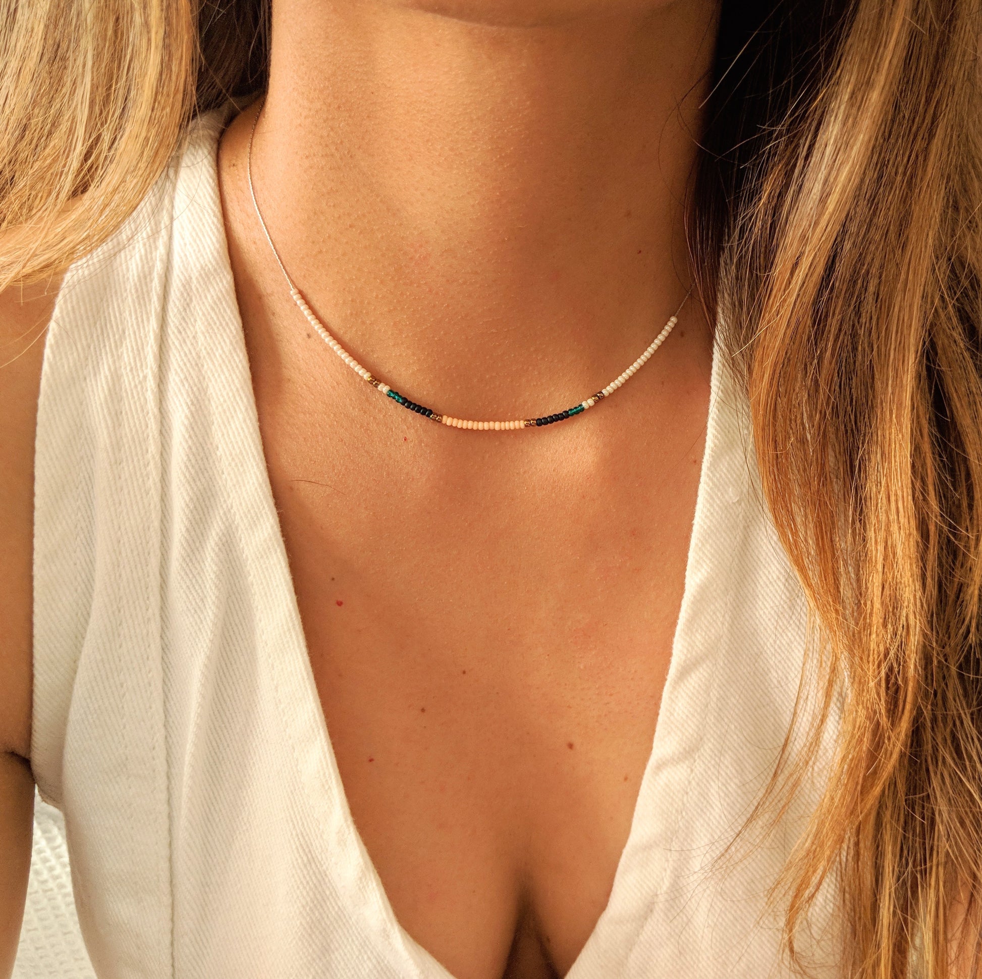 Delicate choker necklace with tiny pastel and dark beads, elegantly displayed on a woman's neck, paired with a white sleeveless blouse for a refined look.