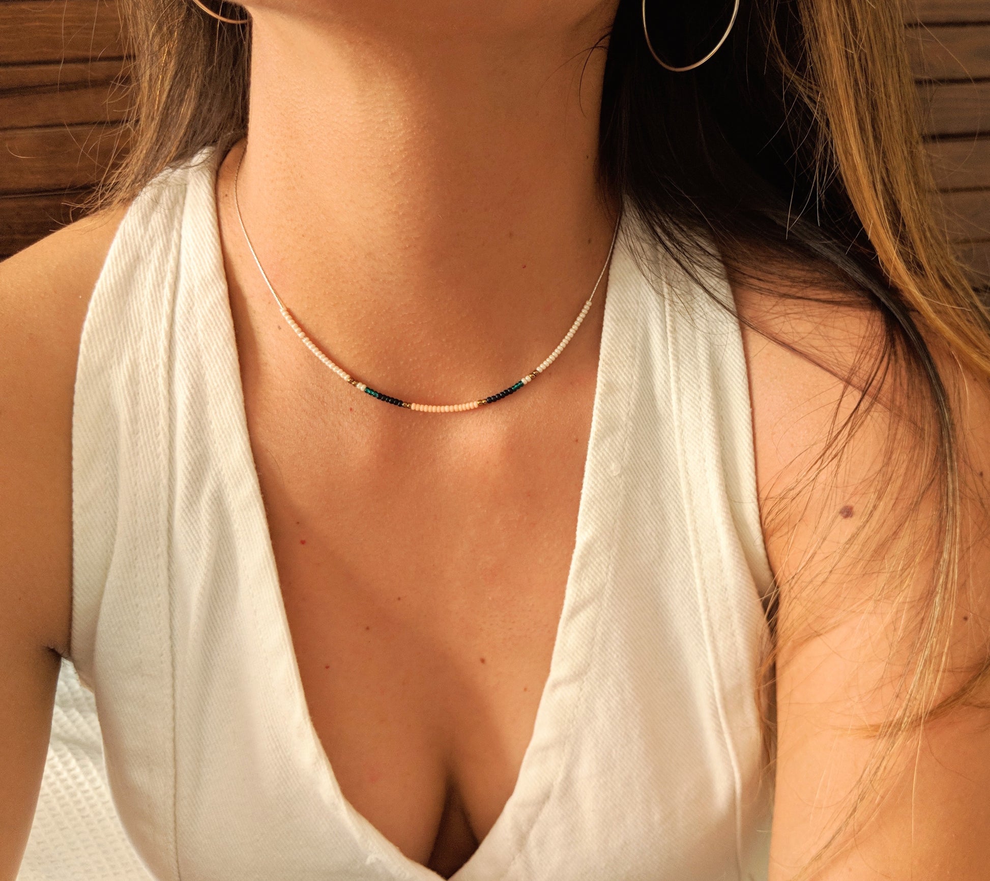 Delicate choker necklace with tiny pastel and dark beads, elegantly displayed on a woman's neck, paired with a white sleeveless blouse for a refined look.